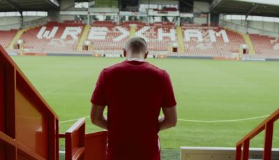 Paul Mullin stands on the steps of the stands facing the team name in 'Welcome to Wrexham' Season 3