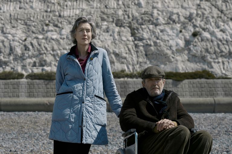 Picture shows: Posed against a white cliff on a stone-covered beach, Marion (Gina McKee) stands beside Patrick (Rupert Everett) who is in a wheelchair.