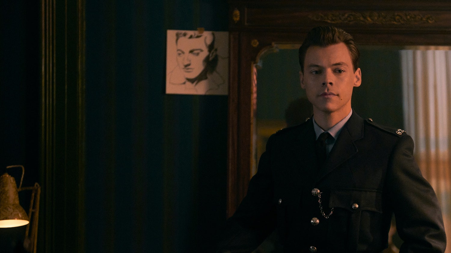 Picture shows: Tom (Harry Styles) in uniform in Patrick's apartment. The room is dark and there is a classical-looking monochrome piece of art on the wall behind him.