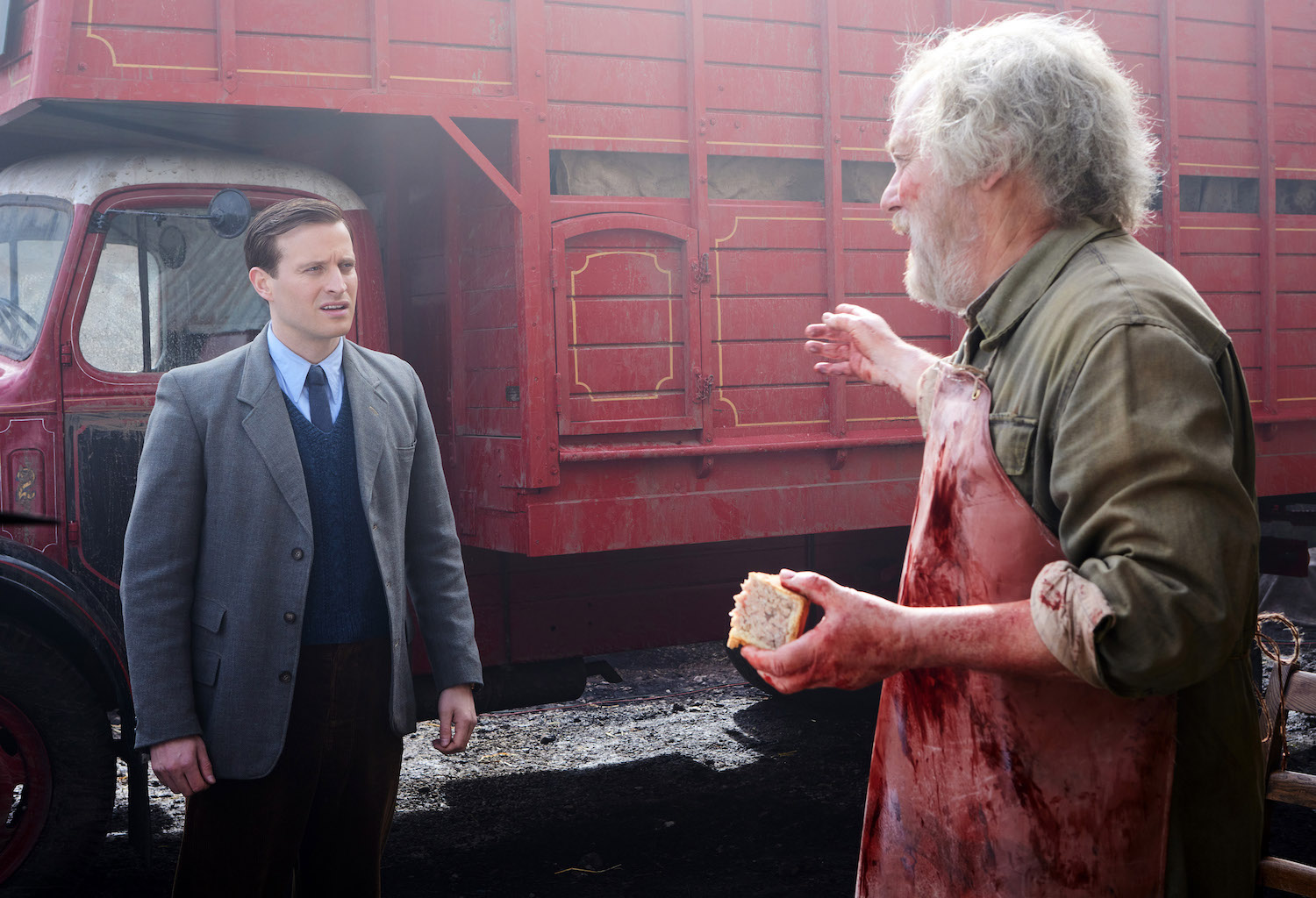 Picture shows: James Herriot (Nicholas Ralph) confronts Jeff Mallock (Jim Moir) about the cow. James is standing in front of Jeff's red truck, inside which the cow is still alive. Jeff, covered as usual in dried blood and other nasty substances, is eating a pork pie which he holds in his left hand.