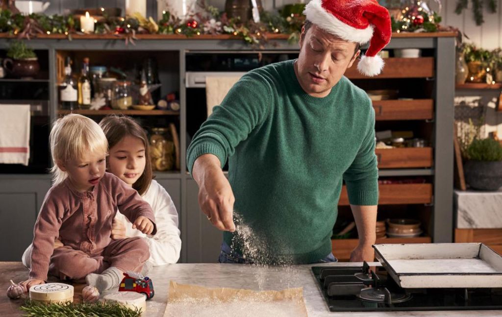 Picture shows: Jamie Oliver wearing a Santa hat sprinkles flour onto baking parchment as his children watch.