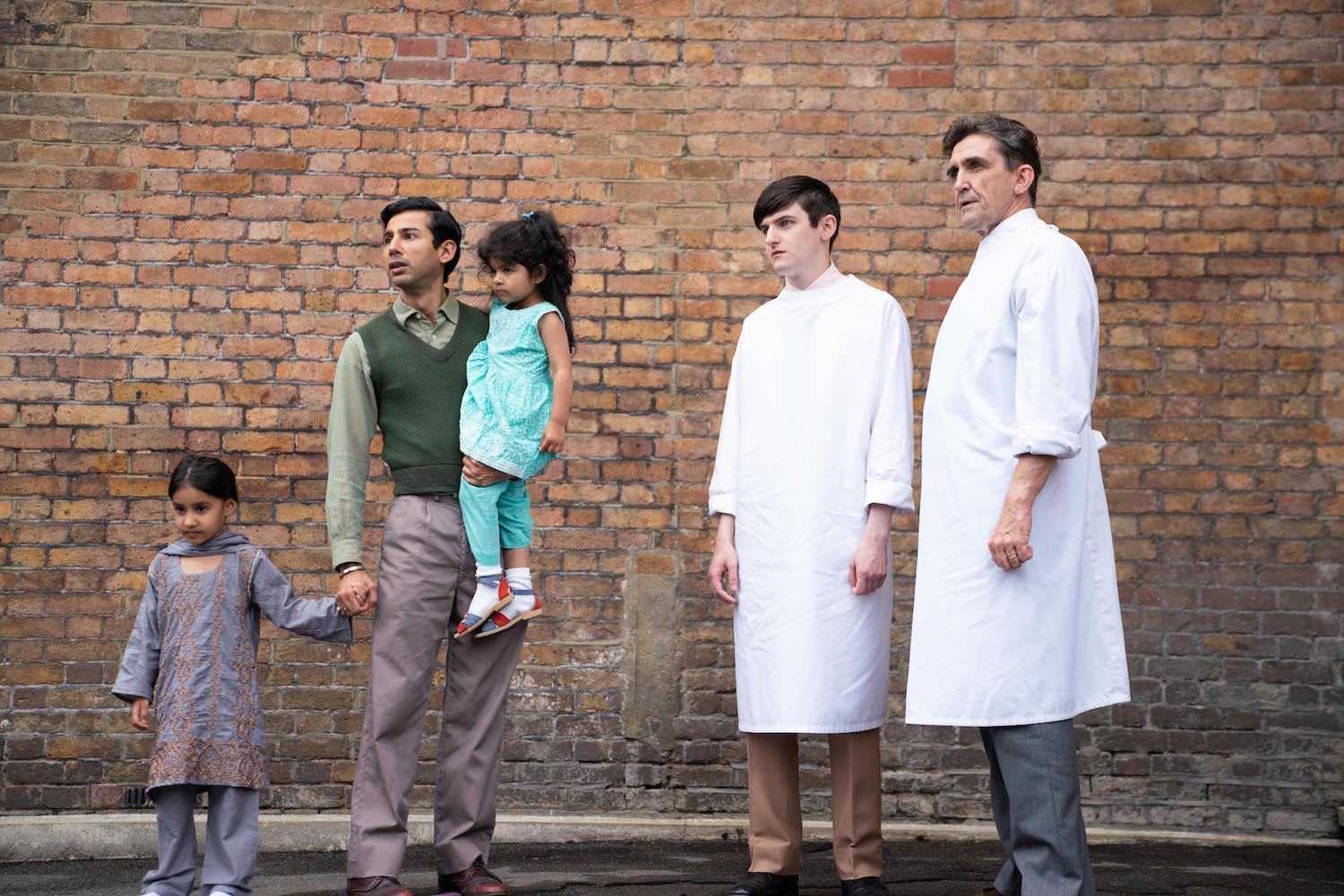 Picture shows: Standing outside against a brick wall, Dr. Turner (Stephen McGann), Tim (Max McMillan),and Romesh (Manish Gandhi) watches the ambulance leave for the hospital, with his critically sick daughter aboard. He holds the hands of his two elder daughters.