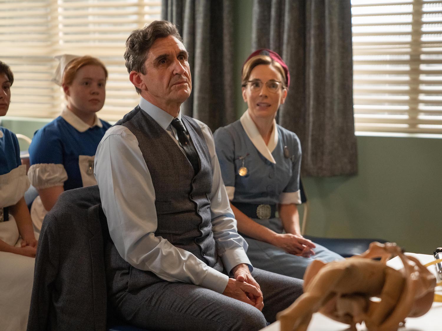 Picture shows: Nurse Shelagh Turner (Laura Main) and Dr Turner (Stephen McGann) sit in the front row at the lecture-demonstration of the ventouse. The device sits on a table in front of them.