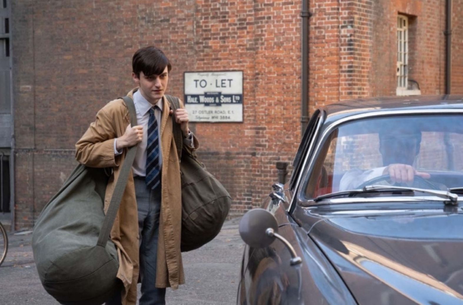 Picture shows: Carrying a huge bag holding cans of hot water and a collapsible bathtub, Tim Turner (Max Macmillan) encounters Matthew Aylward in his car. It's first day as a Bathing Attendant.
