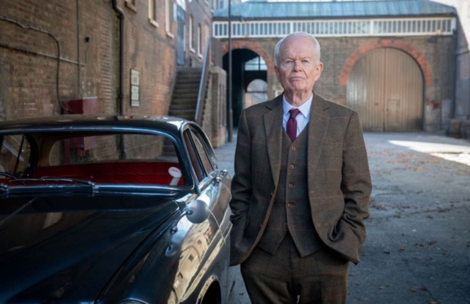 Picture shows: Sir Brigham Aynsley (Michael Cochrane). He's standing beside a shiny car in a courtyard surrounded by brick industrial buildings.
