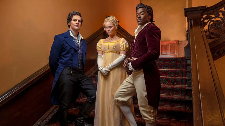 Jonathan Groff, Millie Gibson, and Ncuti Gatwa dressed in Regency era costumes standing on a staircase