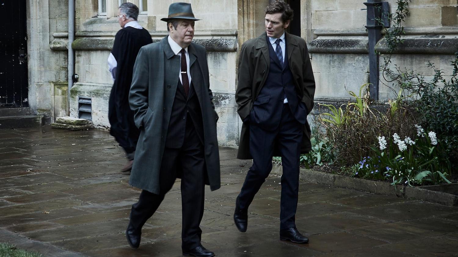 Picture shows: Fred Thursday (Roger Allam) and Morse (Sean Evans). They are walking on wet flagstones beside an old stone building, probably an Oxford college. Ivy and white hyacinths grow in a flower bed.