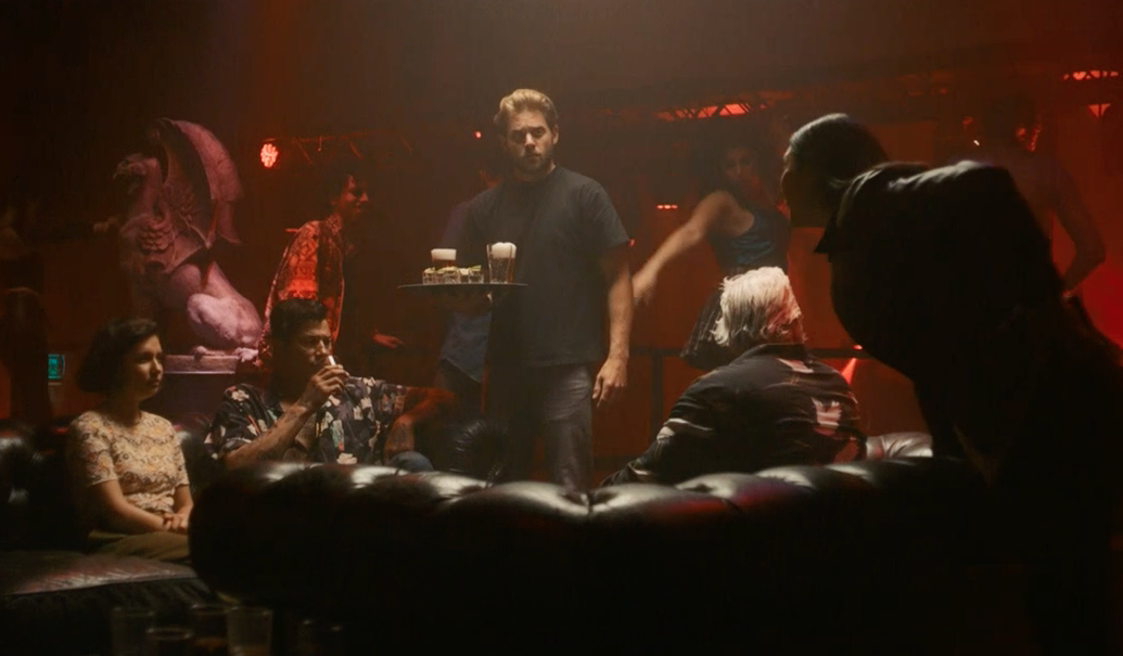 Picture shows: Valentijn Meyer (James Atherton) is serving drinks to nightclub proprietor Hans Lansing (Poal Cairo) and Katja Alsteen (Olivia D’Lima). Hendrik Davie (Darrell D’Silva) sits opposite them on a leather sofa, over which Citra Li (Django Chan-Reeves) leans to question them.
