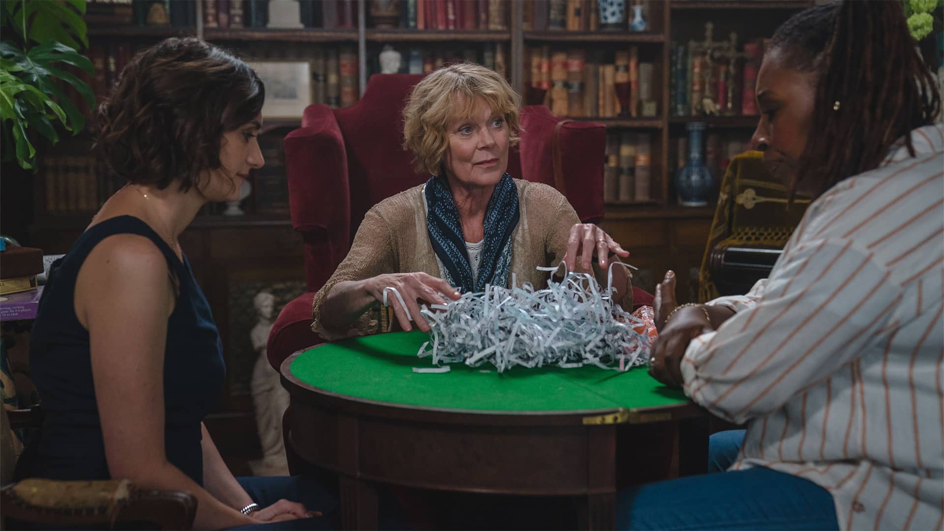 Cara Horgan as Becks Starling, Samantha Bond as Judith Potts, and Jo Martin as Suzie Harris around the library table in 'The Marlow Murder Club' 