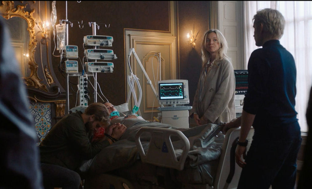 Picture shows: Handcuffed Valentijn Meyer (James Atherton), kneels at the bedside of his sister Mila Manderfeld (Esra Abdioglu) as her heartbeat resumes. Lena Linderman (Loes Haverkort) standing at the other side of the bed, smiles at Van Der Valk (Marc Warren)