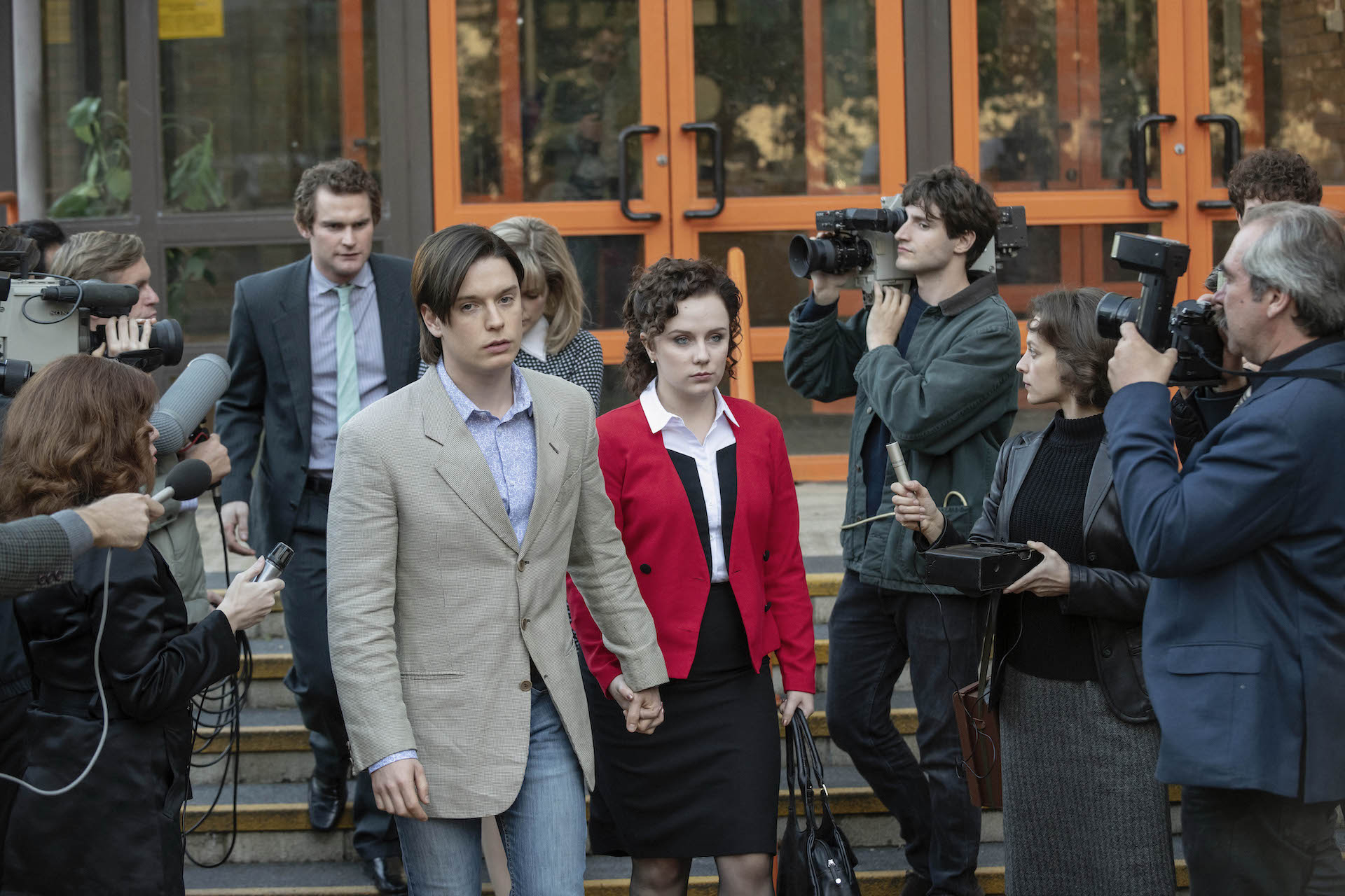 Jeremy Bamber (Freddie Fox), with girlfriend Julie Mugford (Alexa Davies), followed by Colin Caffell (Mark Stanley), puts on his sad face for the press. Is this the face of a murderer? © ITV/HBO-MAX