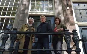 Picture shows: Darrell D'Silva as Hendrik Davie, Marc Warren as Piet Van der Valk, and Maimie McCoy as Lucienne Hassell look down over a railing in 'Van der Valk' Season 3