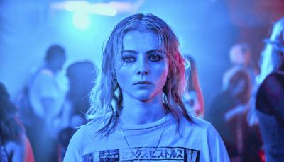 Thomasin McKenzie as Vivian in Totally Completely Fine, standing in a crowded room lit by blue light