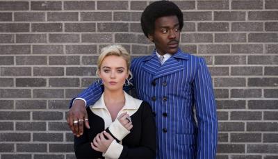 Ncuti Gatwa and Millie Gibson as the Doctor and Ruby Sunday in 1960s period costumes (the Doctor in blue pinstripes and Ruby in a black-and-white mini dress with tall white boots) standing against a brick wall