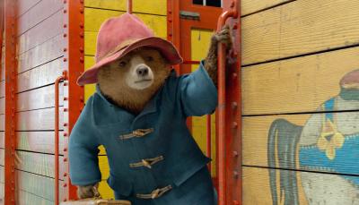 Paddington, dressed in coat and hat, hangs off the side of a train car
