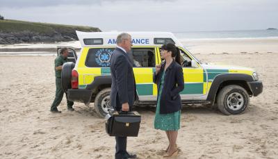 Martin Clunes as Dr. Martin, Caroline Catz as Louisa stand on the beach in front of an ambulance in Doc Martin Season 9