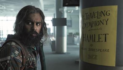 Himesh Patel as Jeevan Chaudhary in front of a Hamlet poster in 'Station Eleven'