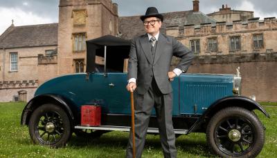Alan Carr stands in front of a 1920s car and estate in Alan Carr's Adventures with Agatha Christie