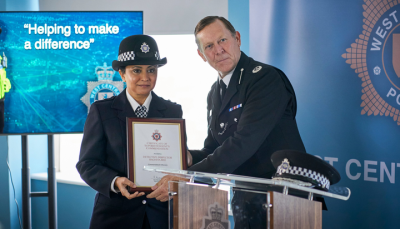 DI Ray in her uniform in front of a screen that reads "helping to make a difference" posing for a photo while being handed an award