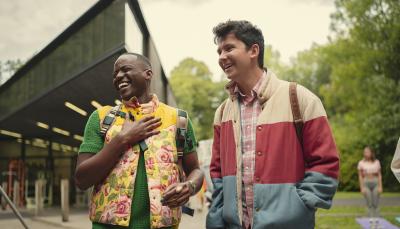 Eric (Ncuti Gatwa) and Otis (Asa Butterfield) stand together outside a school building laughing and smiling