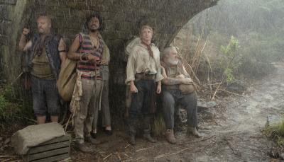 Black Pete (Matthew Maher), Roach (Samba Schutte), Stede (Rhys Darby), and Wee John (Kristian Nairn) shelter under an overpass in the rain, all looking bedraggled.