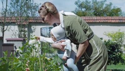 Sandra Hüller as Hedwig Höss holding her baby to smell a flower as Jewish bodies burn yards away in 'The Zone of Interest'