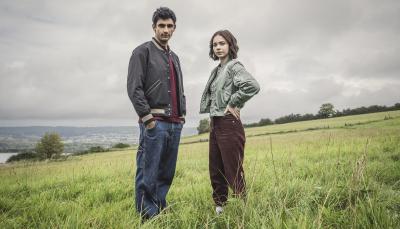 Zain Iqbal as Ravi Singh and Emma Myers as Pip Fitz-Amobi stand in a field in A Good Girl's Guide to Murder
