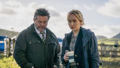 Neill Rea as Detective Senior Sergeant Mike Shepherd, Fern Sutherland as Detective Kristin Sims stare at dinosaur bones and a dead body over coffee in 'The Brokenwood Mysteries'
