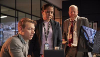 Sam Baker-Jones as DC Liam Payne, Parminder Nagra as DI Rachita Ray, and Steve Oram as DS Clive Bottomley stand around a computer in 'D.I. Ray' Season 2
