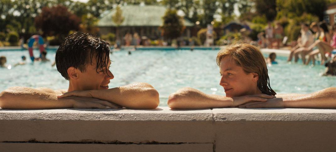 Picture shows: At an outdoor swimming pool Tom (Harry Styles) and Marion (Emma Corrin) smile at each other as they rest their elbows on the edge of the pool.