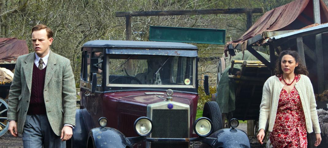 Picture shows: Tristan Farnon (Callum Woodhouse) and Florence Pandhi (Sophie Khan Levy) standing on either side of a 1930s car in a muddy yard