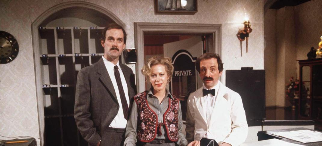 John Cleese as Basil Fawlty, Connie Booth as Polly, and Andrew Sachs as Manuel) in the original 1975 Fawlty Towers