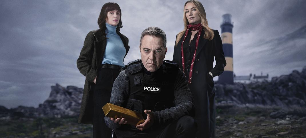 Picture shows: Against the background of a rocky beach with a lighthouse, DCI Tom Brannick (James Nesbitt) kneels, holding a gold ingot. To the left is DI Niamh McGovern (Charlene McKenna) and on the right, Olivia Foyle (Victoria Smurfit). They all look very grim.