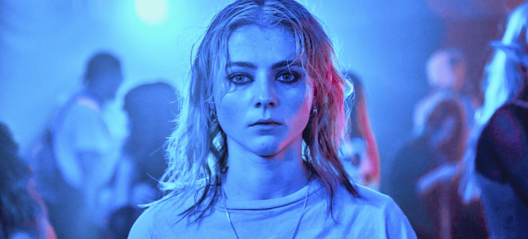 Thomasin McKenzie as Vivian in Totally Completely Fine, standing in a crowded room lit by blue light