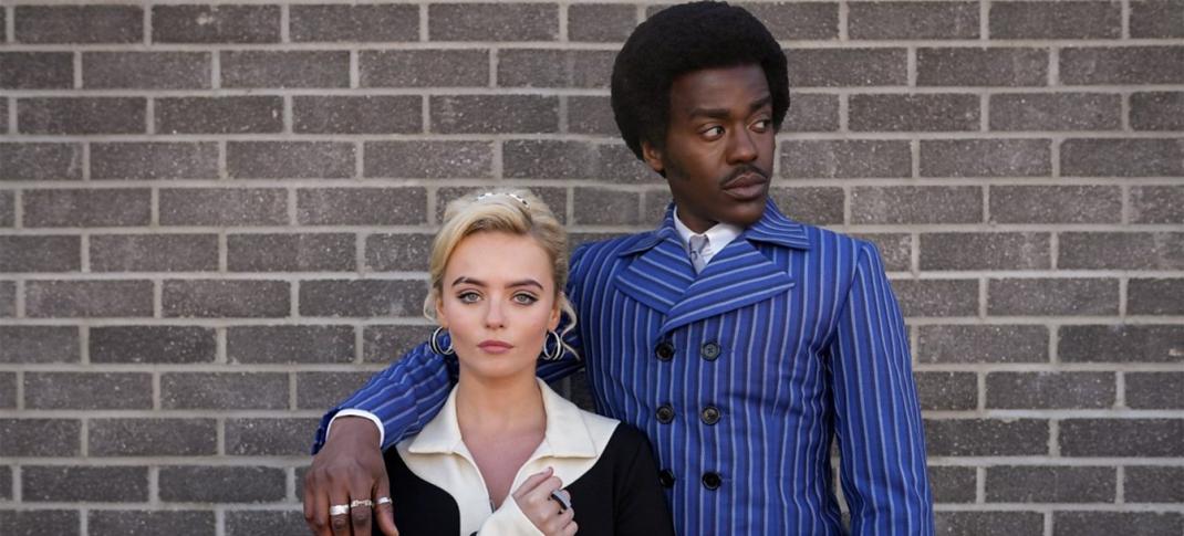 Ncuti Gatwa and Millie Gibson as the Doctor and Ruby Sunday in 1960s period costumes (the Doctor in blue pinstripes and Ruby in a black-and-white mini dress with tall white boots) standing against a brick wall