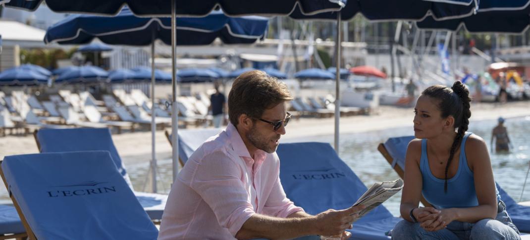 Jamie Bamber as Harry King and Lucie Lucas as Camille Delmasse discuss a case's clues while on the beach in 'Cannes Confidential' Season 1
