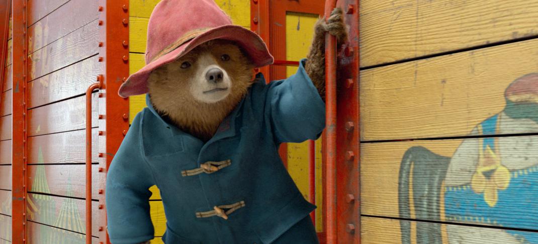 Paddington, dressed in coat and hat, hangs off the side of a train car