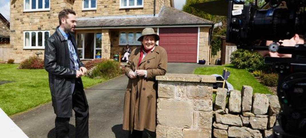 Blethyn and Leon stand casually together in front of a house, smiling at something off camera
