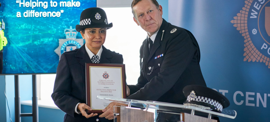 DI Ray in her uniform in front of a screen that reads "helping to make a difference" posing for a photo while being handed an award