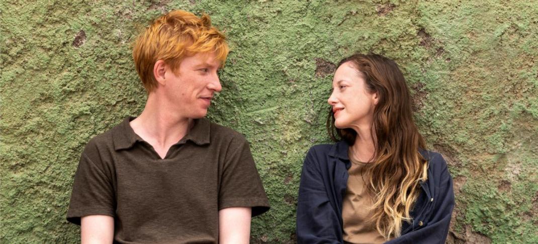 Domhnall Gleeson as Jack and Andrea Riseborough as Alice sit against a wall gazing at each other in 'Alice & Jack'