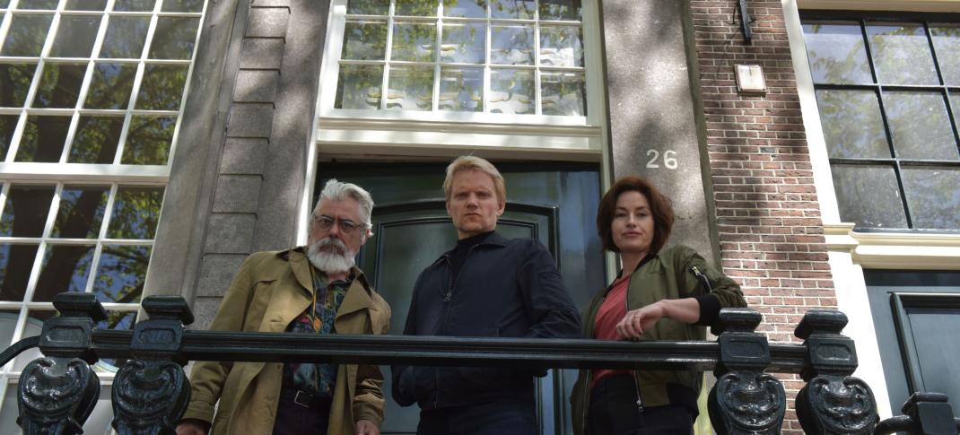 Picture shows: Darrell D'Silva as Hendrik Davie, Marc Warren as Piet Van der Valk, and Maimie McCoy as Lucienne Hassell look down over a railing in 'Van der Valk' Season 3