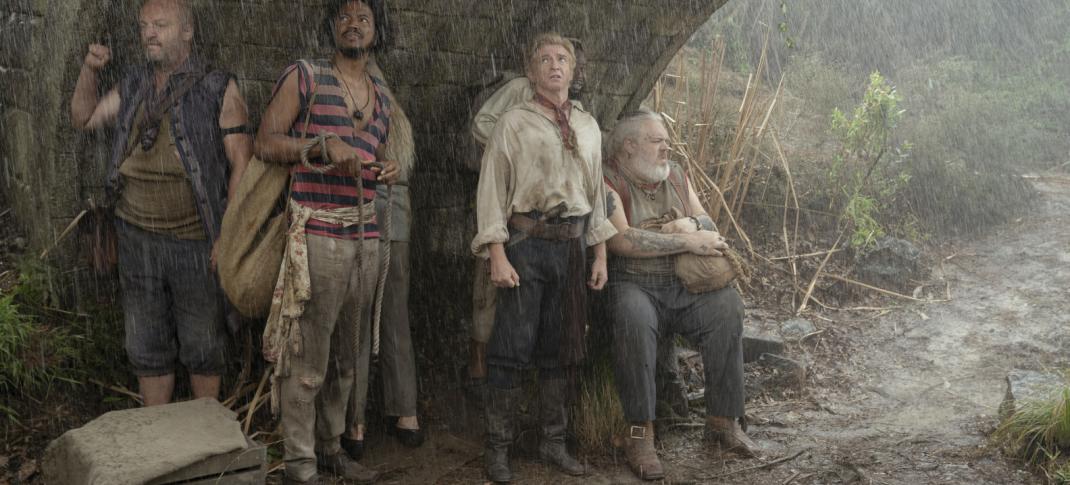 Black Pete (Matthew Maher), Roach (Samba Schutte), Stede (Rhys Darby), and Wee John (Kristian Nairn) shelter under an overpass in the rain, all looking bedraggled.