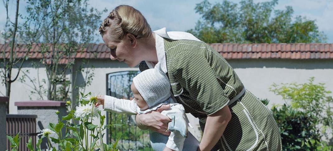 Sandra Hüller as Hedwig Höss holding her baby to smell a flower as Jewish bodies burn yards away in 'The Zone of Interest'