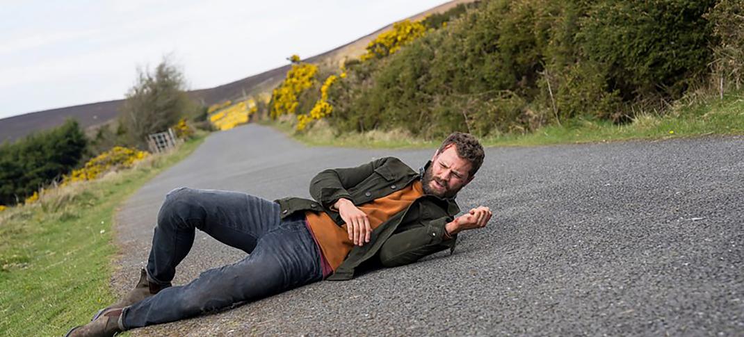 Jamie Dornan as Elliot Stanley lying in the road in 'The Tourist Season 2