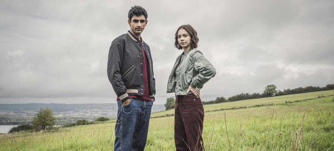 Zain Iqbal as Ravi Singh and Emma Myers as Pip Fitz-Amobi stand in a field in A Good Girl's Guide to Murder