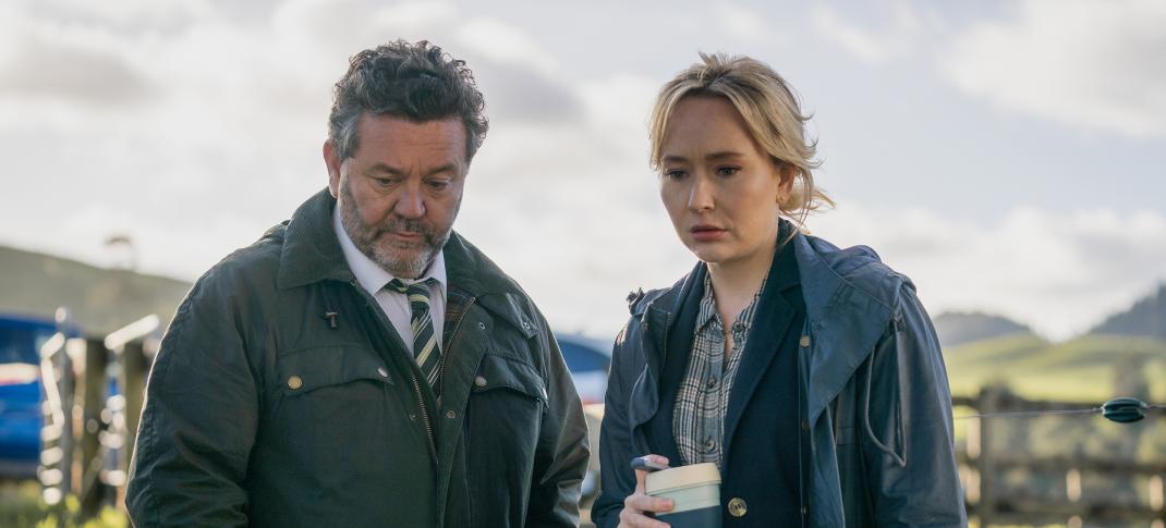 Neill Rea as Detective Senior Sergeant Mike Shepherd, Fern Sutherland as Detective Kristin Sims stare at dinosaur bones and a dead body over coffee in 'The Brokenwood Mysteries'