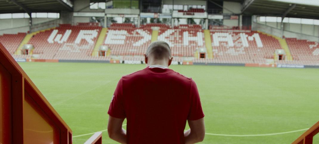 Paul Mullin stands on the steps of the stands facing the team name in 'Welcome to Wrexham' Season 3