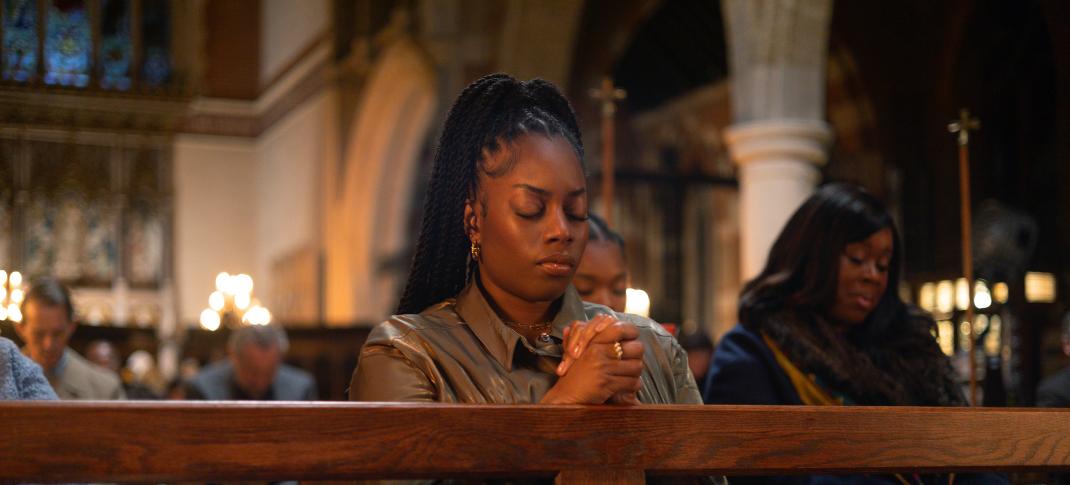 Dionne Brown as Queenie Jenkins, on her knees praying in 'Queenie'