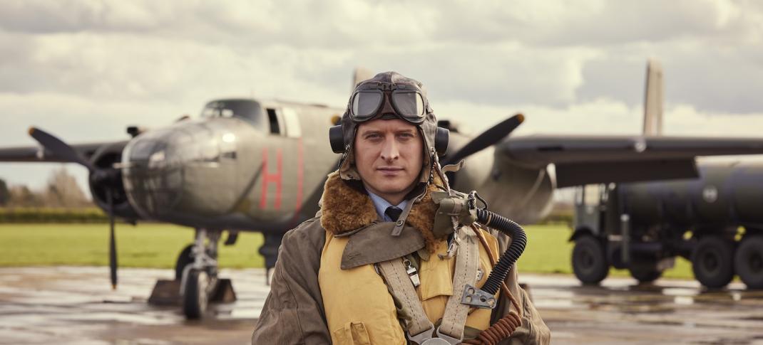 Picture shows: Nicholas Ralph in flying gear on an airfield with planes behind him.